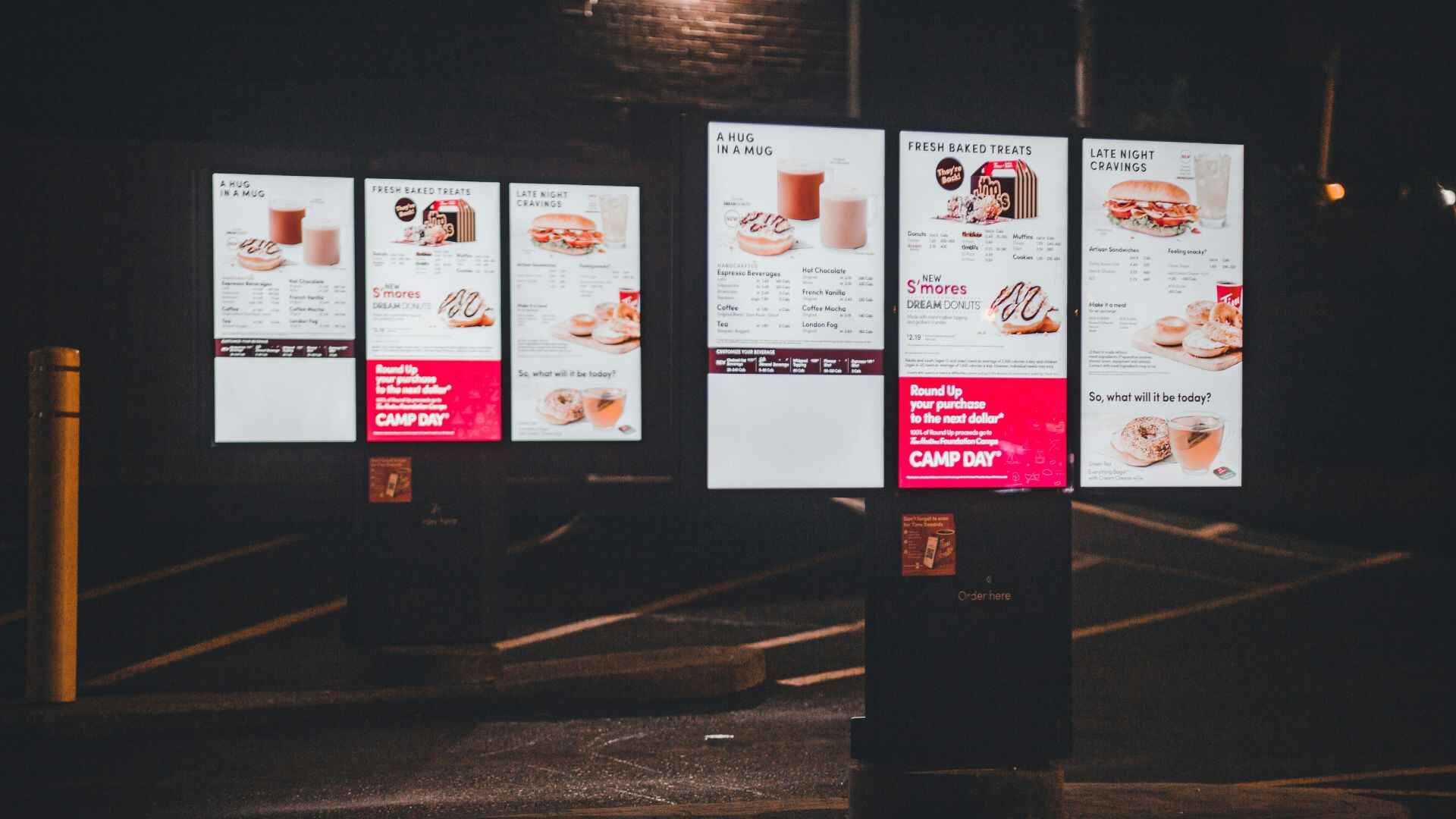 Digital menu boards at a drive-thru restaurant showcasing food items and promotional campaigns under night lighting