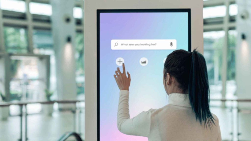 Woman interacting with a digital touchscreen kiosk in a modern retail environment with a search interface displayed
