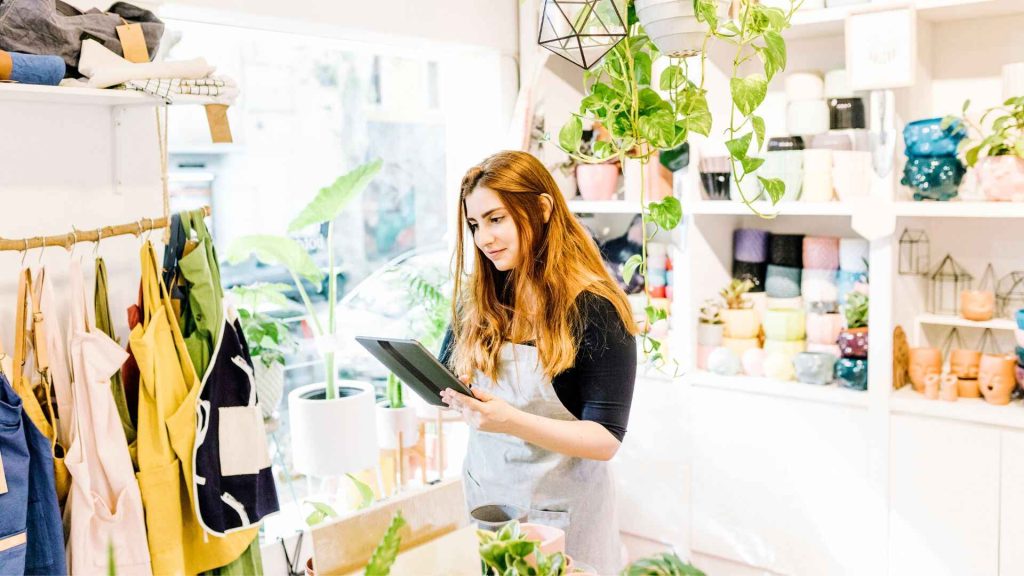 Retail store owner using a tablet in a brightly lit shop with colorful products and plants, showcasing AI-powered retail management