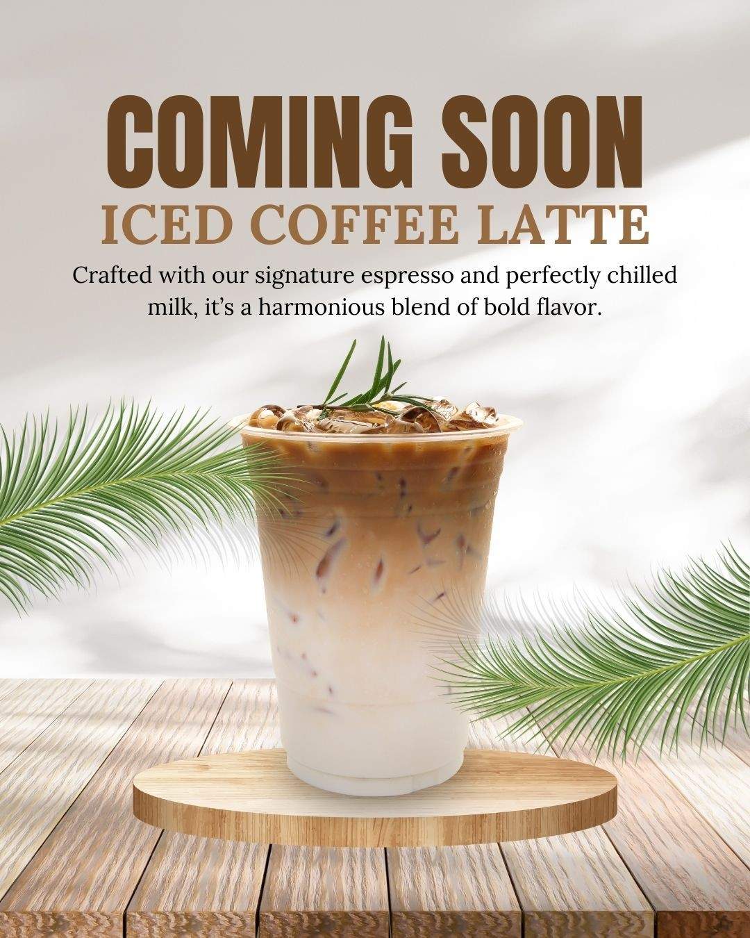 Iced coffee latte in a plastic cup on a wooden platform with tropical leaves and "Coming Soon" text.